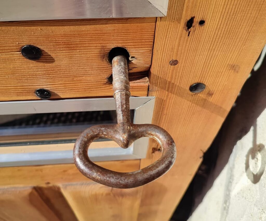 Grosse clé ancienne en fer forgé insérée dans la porte en bois du gîte.